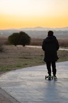 Kid riding a scooter through bike lane at sunset. Calm and relaxing time concept. Copy space.