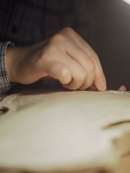artisan working on raw wood violin plate with finger plane on the bench
