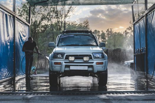 Man on Self-service washes his white suv 4x4 car.