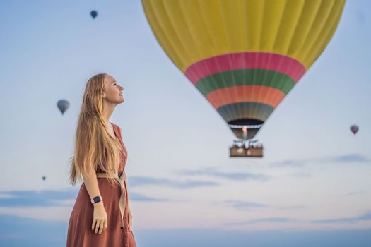 Tourist woman looking at hot air balloons in Cappadocia, Turkey. Happy Travel in Turkey concept. Woman on a mountain top enjoying wonderful view.