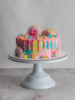 Close up of pink frosted dripping cake with donut and plastel brushed royal star sprinkles insolated on white studio shot