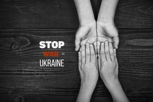 childrens hands holding each other on dark wooden background, with words stop war in ukraine. black and white color. concept needs help and support, truth will win