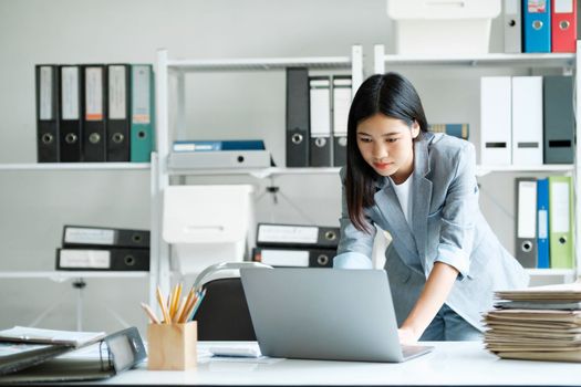 Young asian businesswoman uses a laptop to contact a customer, working hard at the office using laptop data graphs, planning for improvement, analyzing and strategizing for business growth. Business concept