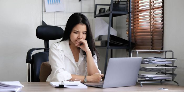 Tired female employee holding head on hand, looking at computer screen, doing hard task, having problem with computer software. Stressed exhausted businesswoman suffering from headache, feeling bored