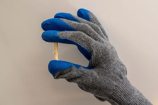 A worker's hand in a protective glove holds a plastic dowel pin on a white background. renovation in the bathroom. installation of bathroom accessories.