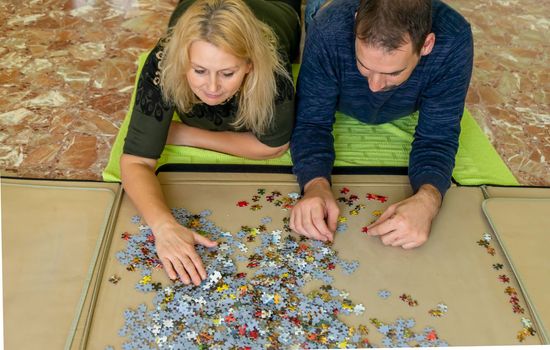 Adorable couple doing a puzzle lying on the floor, they enjoy their company while spending some fun time together