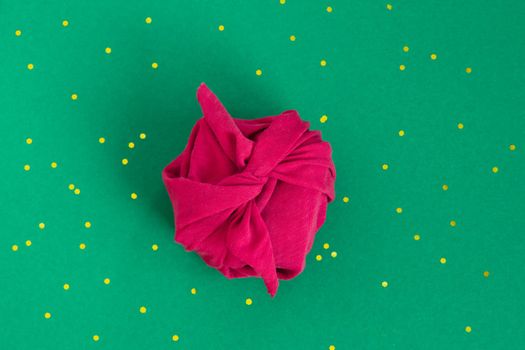 Paper free gift wrapping technique Furoshiki. Viva magenta fabric on green background. Flat lay, present box, top view. Christmas, valentines, new year concept