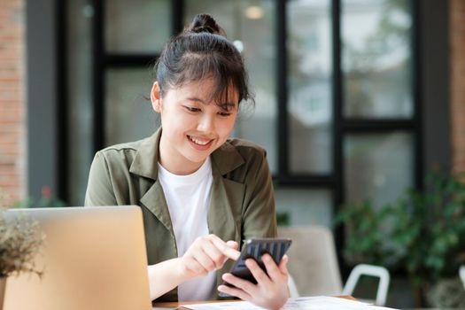 Young asian businesswoman uses a mobile phone to contact a customer, working hard at the office using laptop data graphs, planning for improvement, analyzing and strategizing for business growth. Business concept