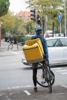 Cyclist Delivery food man waiting with a bike traffic light to cross working on the streets of Madrid. Sustainability and ecology concepts