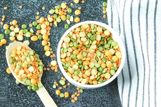 Yellow and green peas in white bowl on a napkin and a gray stone background. Different types of peas, close up, top view.