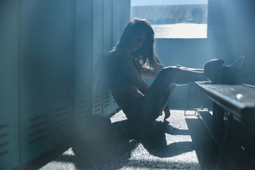Young girl of an athletic build in the locker room of a sports club wears boxing gloves, a girl is dressed in sports black underwear, sun rays from window, sneakers. High quality photo