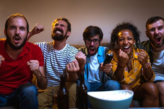 Group of friends watching football game on tv celebrating teams scoring goal. Soccer. Looking at camera. Leisure activities concept.