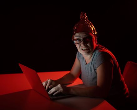 Paranoid caucasian woman typing on a computer wearing a tinfoil cap. Conspiracy theory