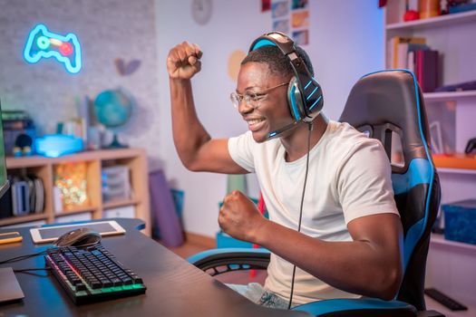 Cybersport young pro gamer happy with winning the game, feel exited, show YES hand gesture, celebrates victory in online game competition. Side view. Guy playing video game at home in his room. High quality photo