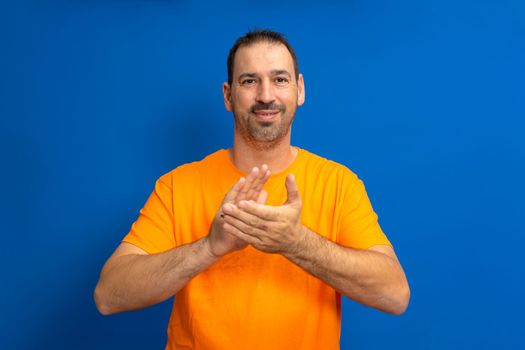 Hispanic handsome elegant man over blue isolated background.Clauping and clapping happy and joyful, smiling proud hands together.