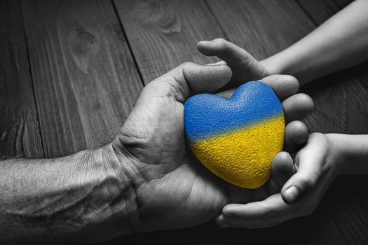 hand holds yellow and blue heart on dark wooden background. black and white color. concept needs help and support, truth will win