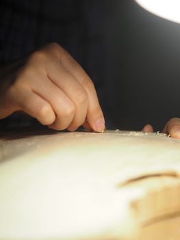 artisan working on raw wood violin plate with finger plane on the bench