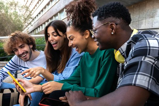 Multiracial college student friends look at mobile phone laughing together. Group of happy people using smartphone outdoors. Youth lifestyle and social media addiction concept.