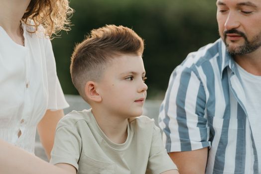 Father, mother, and son are sitting on the steps in the garden of an old European town. A close photo of a little boy with his smiling family in the park in summer at sunset