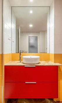 New empty bathroom with yellow tiles and round sink on red furniture.