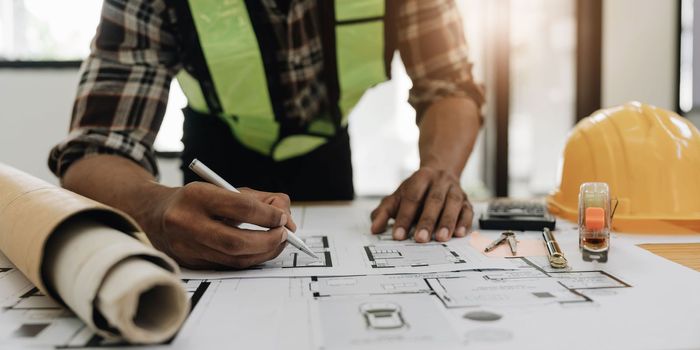 Close up of civil male engineer asian working on blueprint architectural project at construction site at desk in office