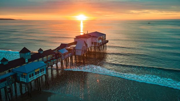 Image of Maine beach ocean waves at sunrise with old wood pier covered in shops