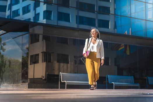 Business woman walking in a modern city. Elegant white jacket and yellow pants. Laptop and technology. High quality photo