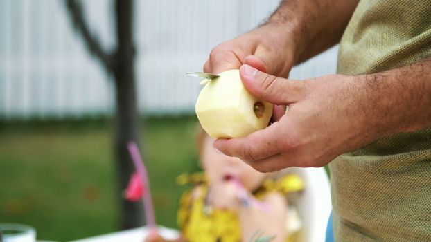 summer, in the garden, slow motion, close-up, men's hands, peel an apple with a knife, cut the peel. High quality photo