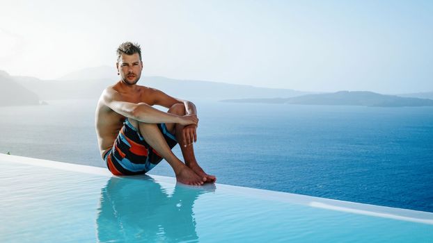 Santorini Greece Oia, young men in swim shorts relaxing in the pool looking out over the caldera of Santorini Island Greece, infinity pool, a young guy on a luxury vacation in Europe Greece