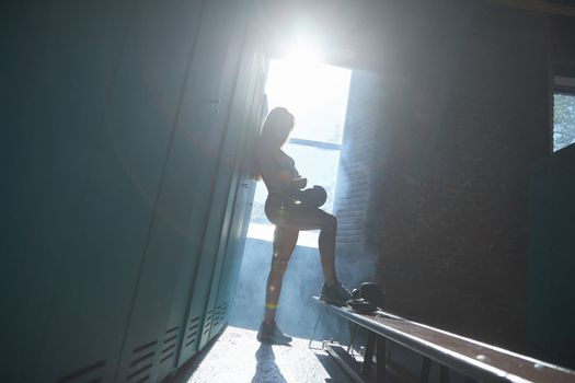 Young girl of an athletic build in the locker room of a sports club wears boxing gloves, a girl is dressed in sports black underwear, sun rays from window, sneakers. High quality photo