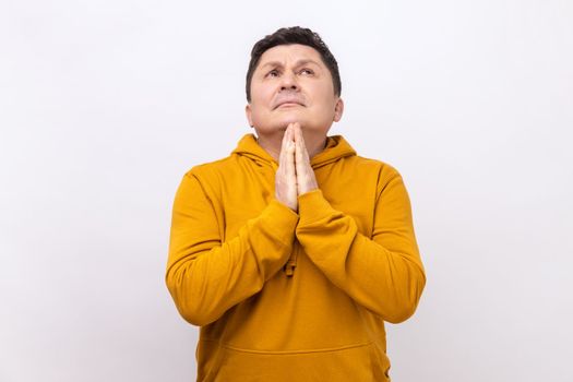 Portrait of handsome middle aged man praying up heartily, feeling guilty, pleading begging help from heaven, wearing urban style hoodie. Indoor studio shot isolated on white background.