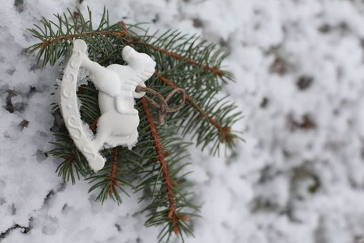 Christmas toy horse hanging on a green branches in the snow in winter. Christmas tree, toy horse, gift. New Year decor.