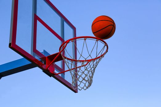 A basketball ball flies into a basket on an open basketball court. Basketball against the sky.