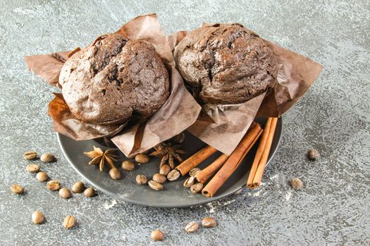 Homemade delicious chocolate cupcake muffin on a black plate and light gray stone background with spices