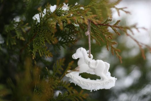 Christmas toy horse hanging on a green branches in the snow in winter. Christmas tree, toy horse, gift. New Year decor.