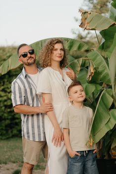 Father, mother, and son are hugging near the palm trees in the tropical country. A happy family in the garden in summer at sunset.