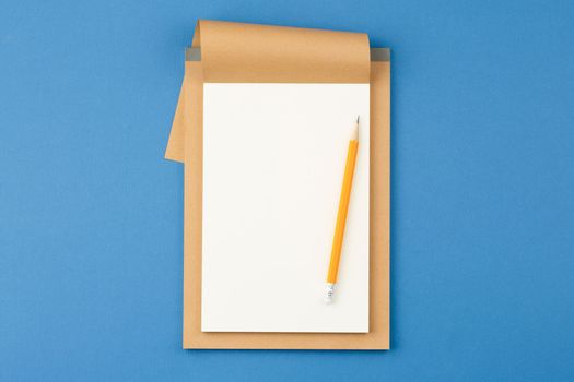Open notebook with white blank sheet and pencil on blue isolated background. Top view.