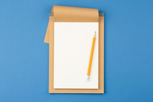 Open notebook with white blank sheet and pencil on blue isolated background. Top view.