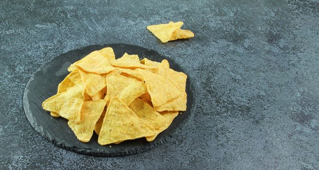 Mexican chips nachos. Black stone plate with corn chips nachos on the black concrete background. Top view. Banner