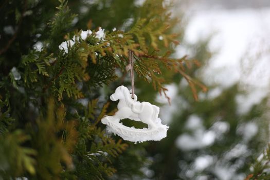 Christmas toy horse hanging on a green branches in the snow in winter. Christmas tree, toy horse, gift. New Year decor.