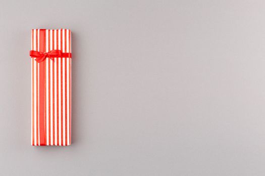 Present in striped paper with red satin bow on gray isolated background. Flat lay. Gift box with satin red bow. Top view.