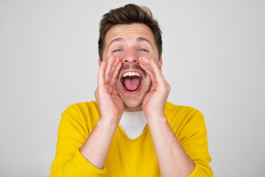 Excited young caucasian man shouting with hands cupped around mouth. Listen to this wonderful news.