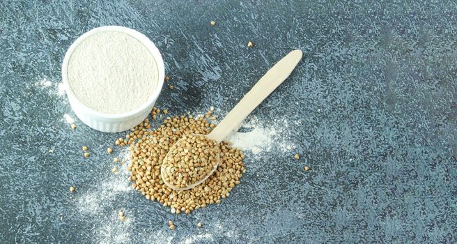 Buckwheat flour in a white bowl and wooden spoon, raw green buckwheat grain on concrete stone background, close up, top view. Alternative flour, gluten free flour, healthy nutrition, banner
