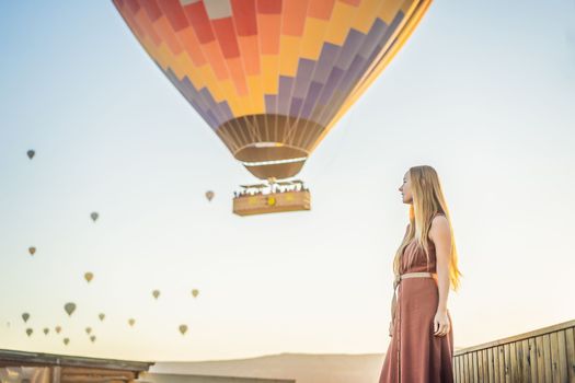 Tourist woman looking at hot air balloons in Cappadocia, Turkey. Happy Travel in Turkey concept. Woman on a mountain top enjoying wonderful view.
