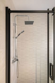 Modern tiled bathroom with rain head, hand held shower and glass door with black framing