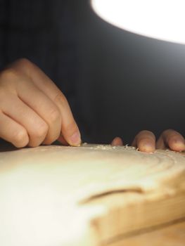 artisan working on raw wood violin plate with finger plane on the bench