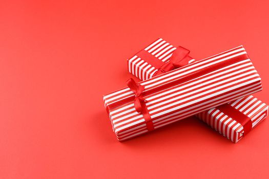 Gifts in striped wrapping paper with red bow on red isolated background. Present boxes