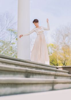 beautiful slim woman in a long evening dress stands at the columns.