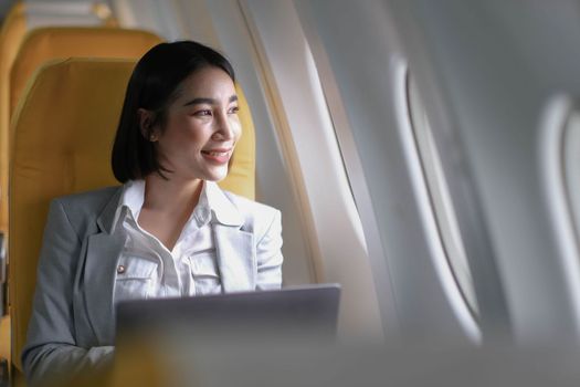 Joyful asian woman sits in the airplane and using laptop while go to travel..