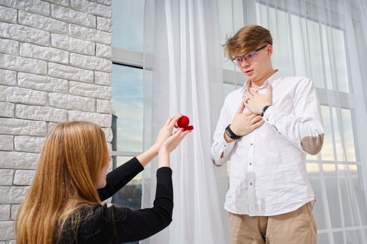Embarrassing moment. Romantic concept. Young woman holding box with engagement ring, making marriage proposal to her boyfriend indoors, women psychology.